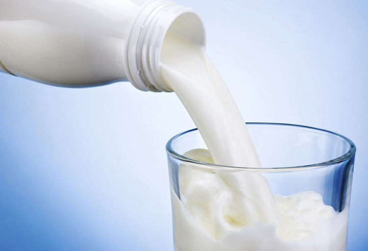 Pouring milk from white plastic bottle into glass on blue